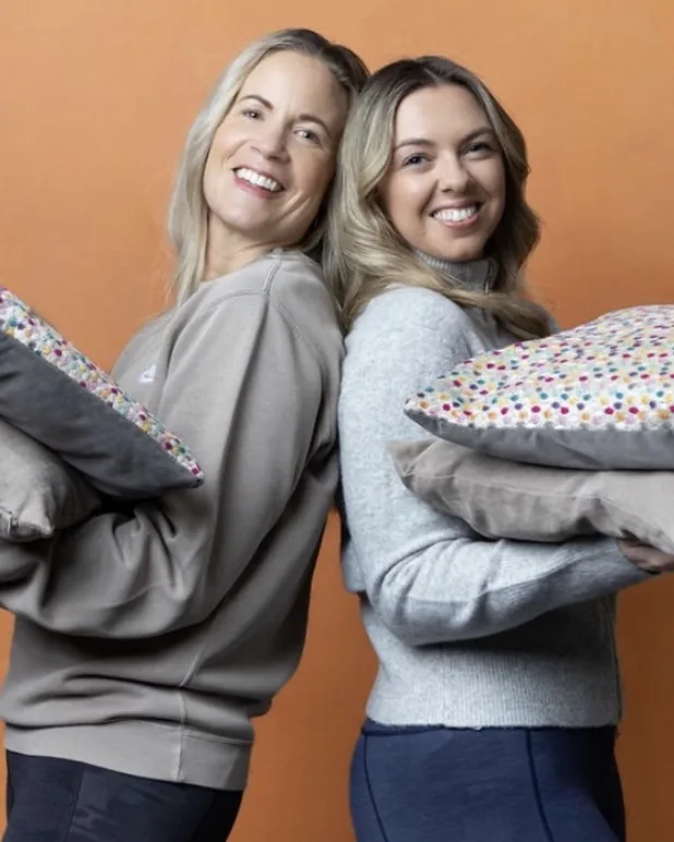 Jane and Alicia from Life Laundry, back to back, holding cushions and laughing